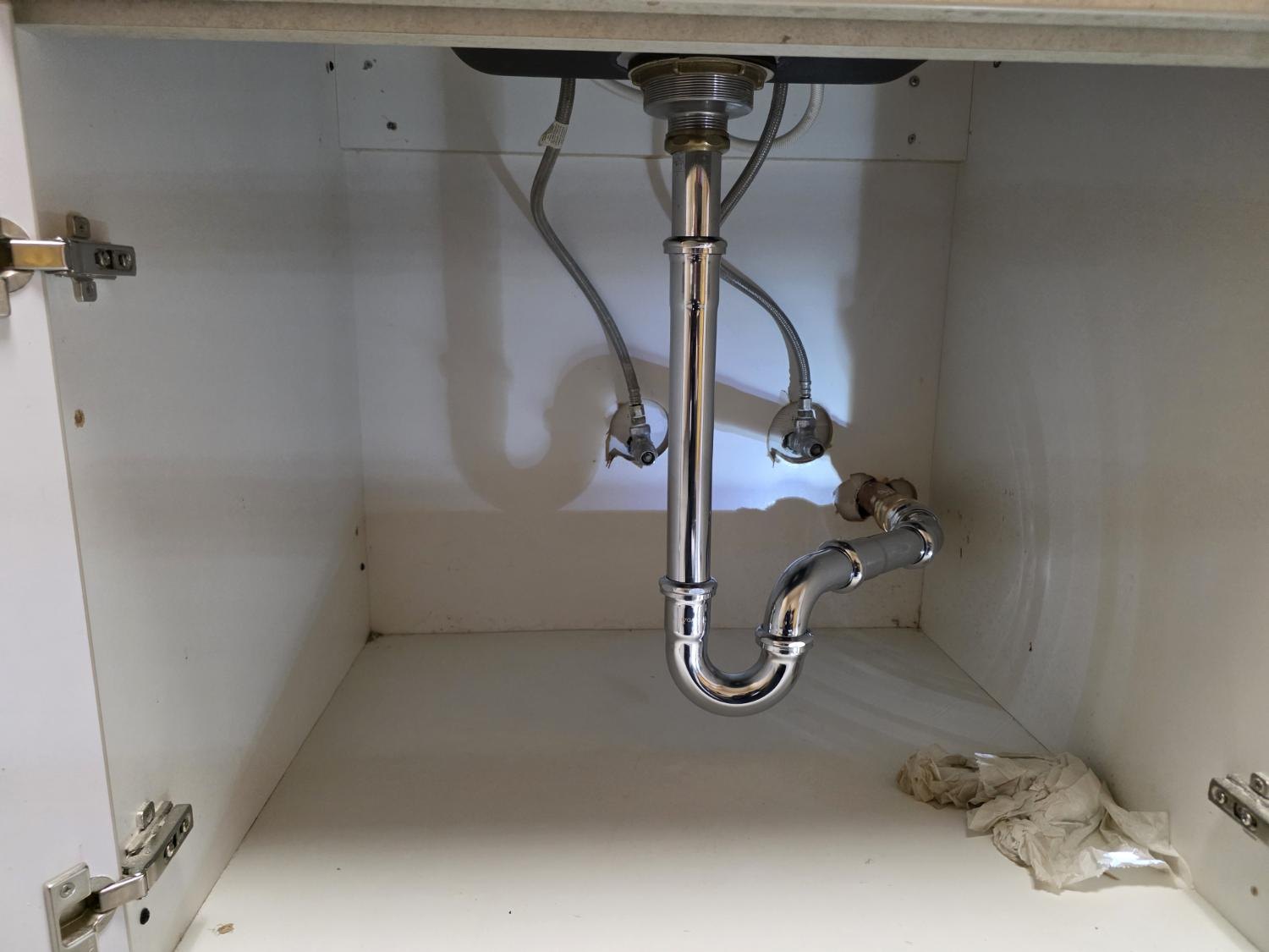 Under-sink cabinet after work: new chrome P-trap and supply lines connected