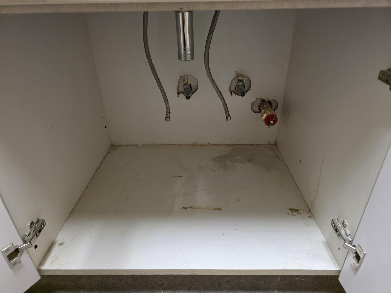 Under-sink cabinet before work: drain disconnected and supply lines hanging